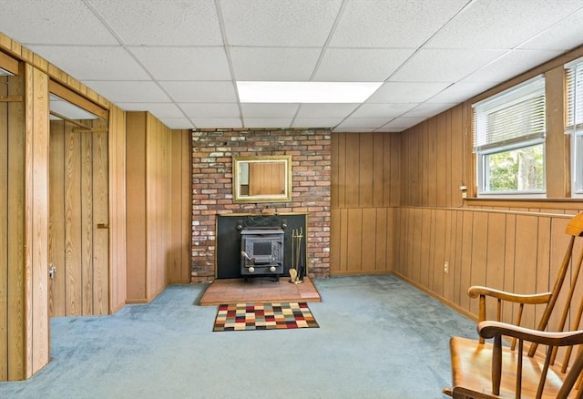 unfurnished room with carpet floors, a wood stove, wooden walls, and a paneled ceiling