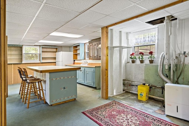 kitchen featuring freestanding refrigerator, open shelves, a kitchen island, a kitchen breakfast bar, and a drop ceiling