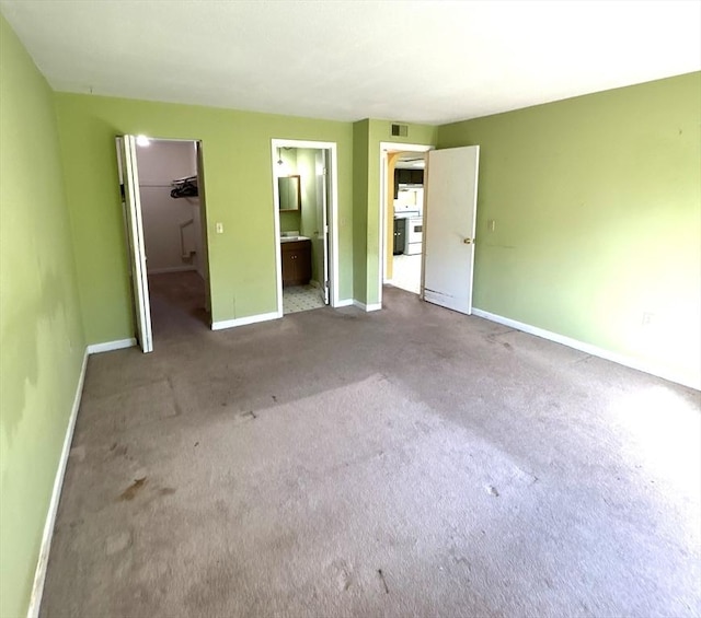 unfurnished bedroom featuring carpet floors, a closet, baseboards, a spacious closet, and ensuite bath