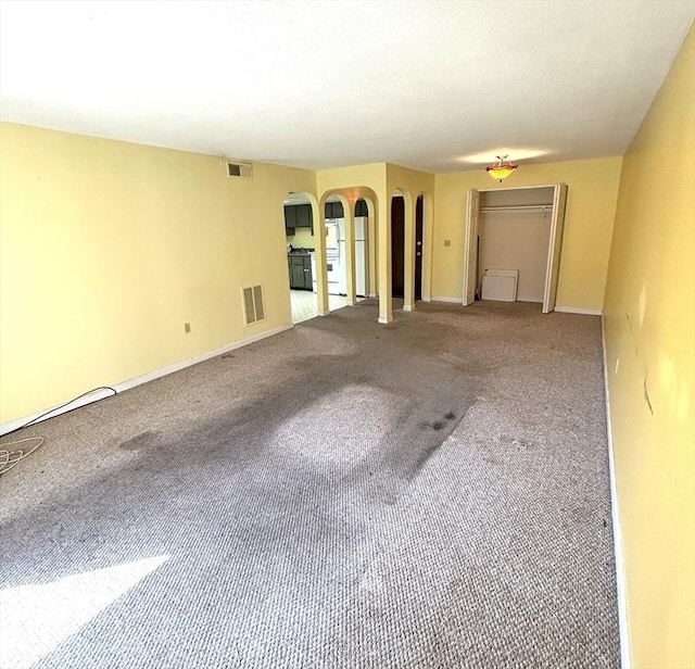 unfurnished living room with arched walkways, baseboards, visible vents, and carpet