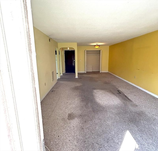 carpeted spare room featuring arched walkways, baseboards, visible vents, and a textured ceiling