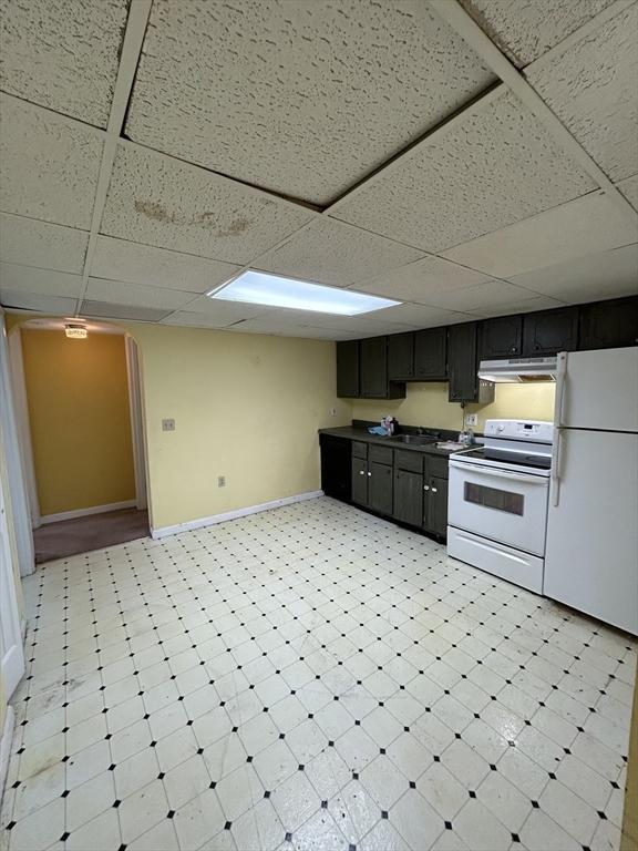kitchen with white appliances, under cabinet range hood, a paneled ceiling, and light floors