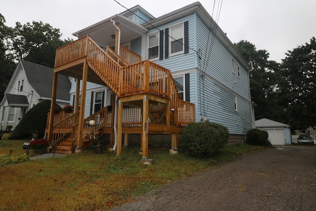 back of property with a garage, a deck, a yard, and an outbuilding