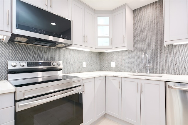 kitchen with decorative backsplash, light stone counters, stainless steel appliances, sink, and white cabinets