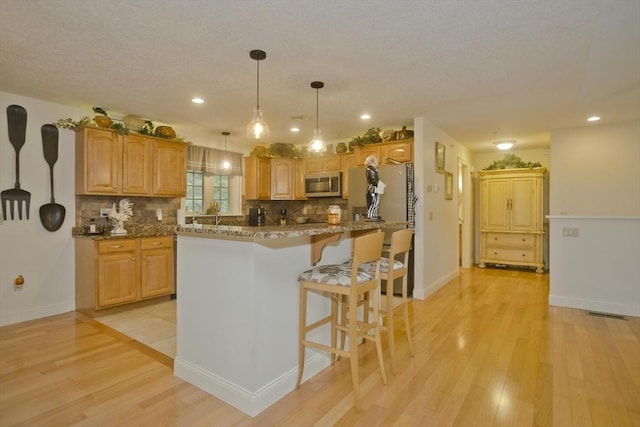 717 Northampton St Unit 41, Holyoke, MA 01040 - kitchen featuring stainless steel microwave, decorative backsplash, light wood-style floors, a breakfast bar area, and hanging light fixtures