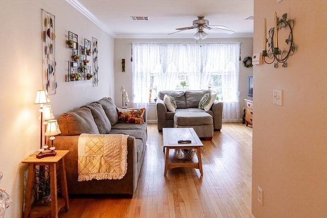 living area featuring visible vents, a ceiling fan, light wood finished floors, and crown molding