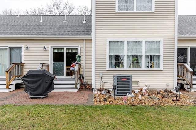 rear view of house with a lawn, central AC unit, a patio area, a shingled roof, and entry steps