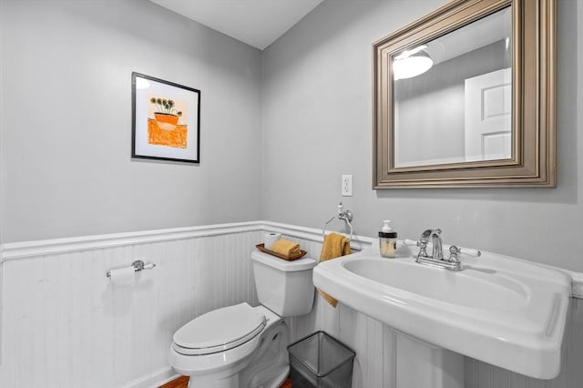 bathroom featuring a wainscoted wall, toilet, and a sink