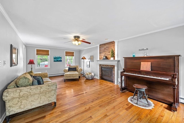 living room featuring crown molding, wood finished floors, baseboard heating, a ceiling fan, and a large fireplace
