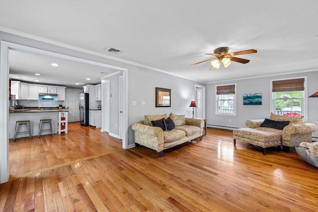 living room featuring a baseboard heating unit, light wood finished floors, ceiling fan, crown molding, and recessed lighting