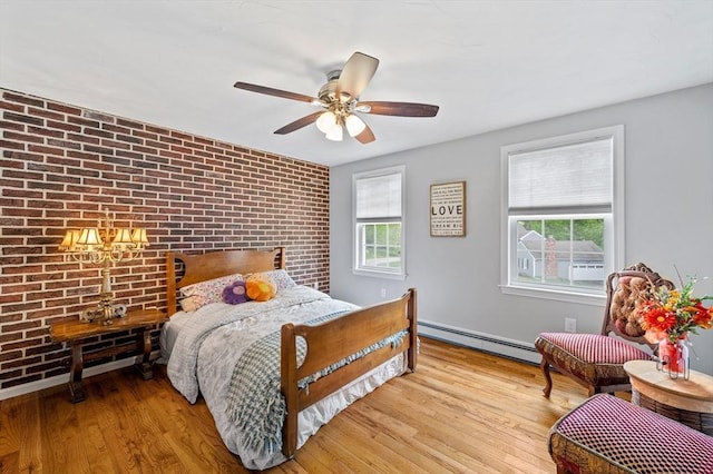 bedroom with a baseboard heating unit, brick wall, wood finished floors, and a ceiling fan