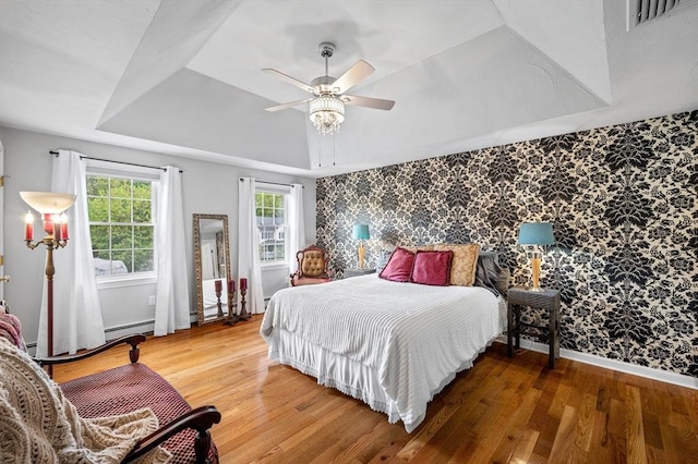 bedroom with wallpapered walls, an accent wall, a tray ceiling, wood finished floors, and baseboards