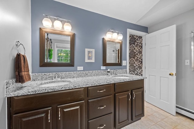bathroom with tile patterned flooring, a baseboard heating unit, vaulted ceiling, and double vanity