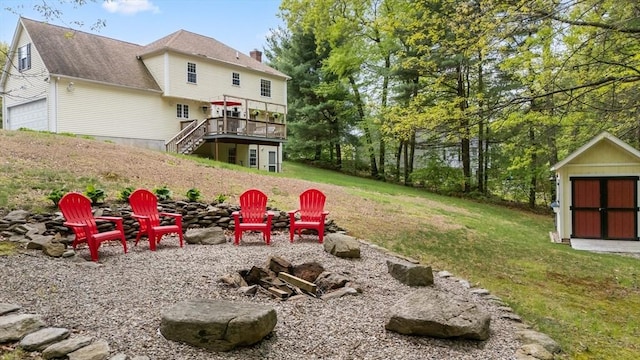 view of grassy yard featuring an outdoor fire pit, stairway, a wooden deck, a storage shed, and an outbuilding