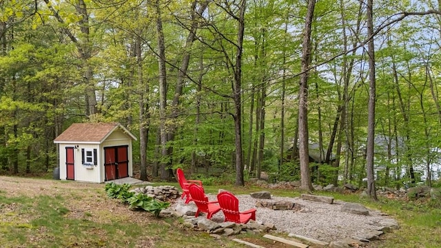 view of yard with an outdoor fire pit, a storage unit, an outbuilding, and a forest view