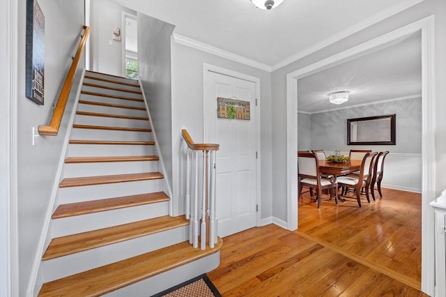 staircase with wood finished floors, ornamental molding, and baseboards