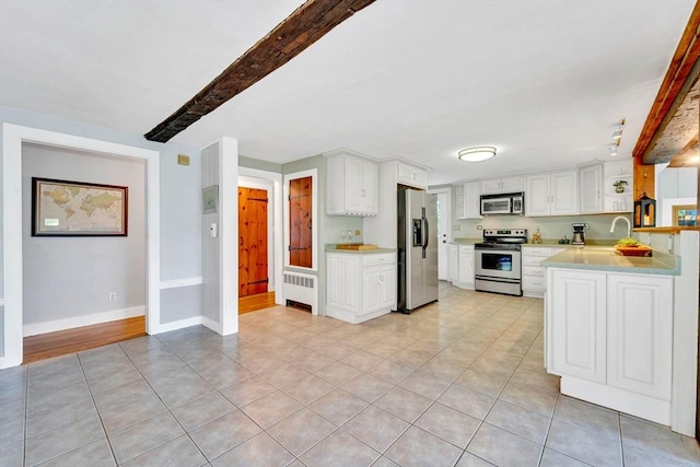 26 Beacon St, Amesbury, MA 01913 - kitchen with appliances with stainless steel finishes, radiator, light countertops, white cabinetry, and beamed ceiling