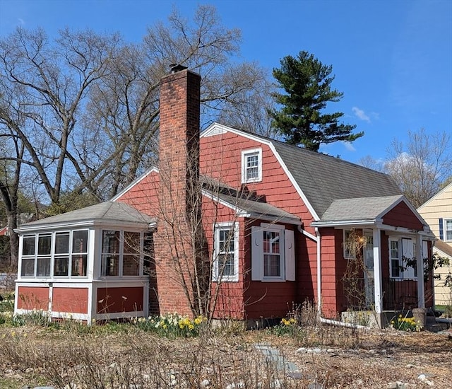 exterior space with a sunroom, a shingled roof, and a chimney
