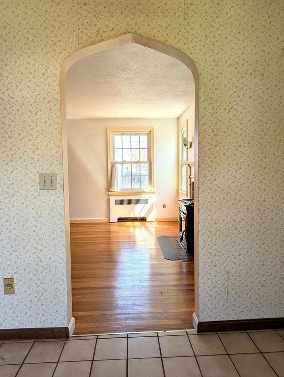 hallway with arched walkways, radiator heating unit, wallpapered walls, and a textured ceiling