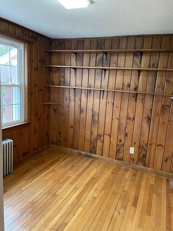 empty room with a wealth of natural light, hardwood / wood-style flooring, and radiator heating unit