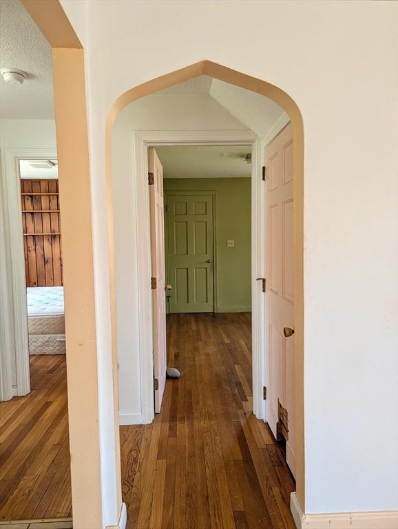 corridor featuring arched walkways, dark wood-style flooring, and baseboards