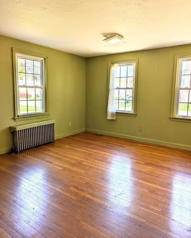 spare room featuring baseboards, radiator, a textured ceiling, and hardwood / wood-style flooring