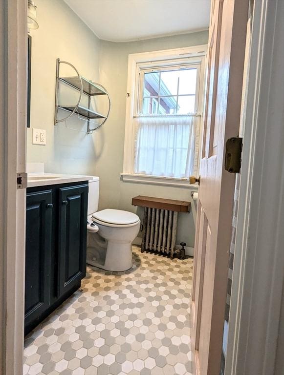 half bath with toilet, radiator heating unit, and vanity