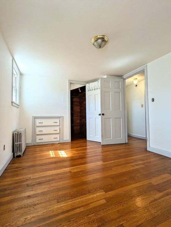 unfurnished bedroom with baseboards, radiator, a closet, and wood finished floors