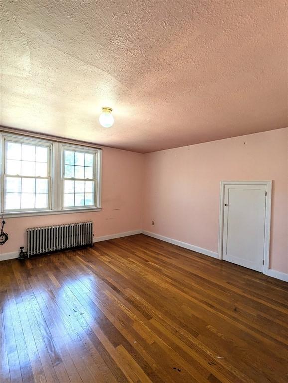 unfurnished room with a textured ceiling, baseboards, dark wood-style floors, and radiator heating unit