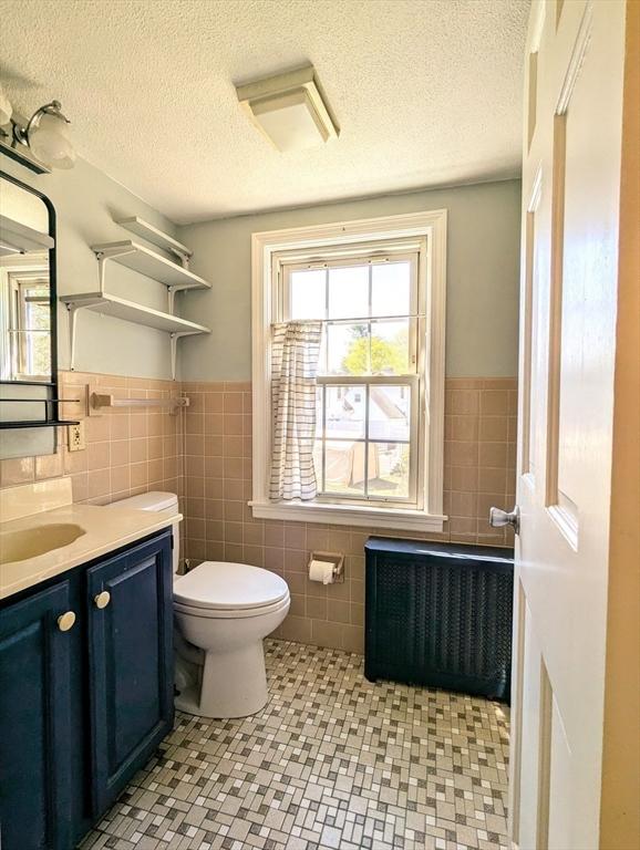 bathroom featuring tile walls, toilet, radiator heating unit, vanity, and a wainscoted wall