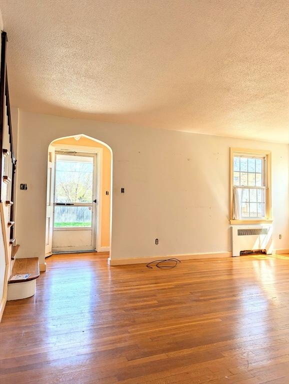 unfurnished room with radiator, a textured ceiling, wood finished floors, and arched walkways