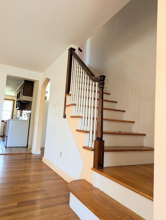 staircase featuring arched walkways, baseboards, washer / clothes dryer, and wood finished floors