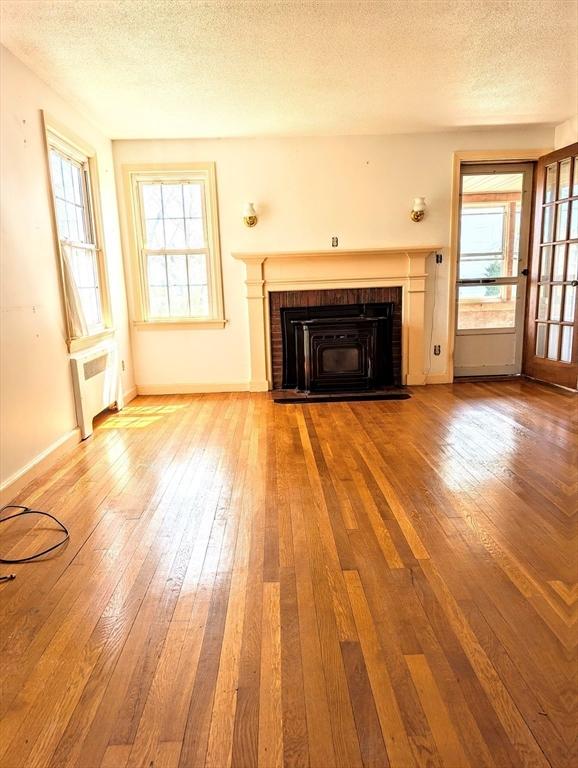 unfurnished living room featuring hardwood / wood-style flooring, radiator heating unit, a textured ceiling, a fireplace, and baseboards