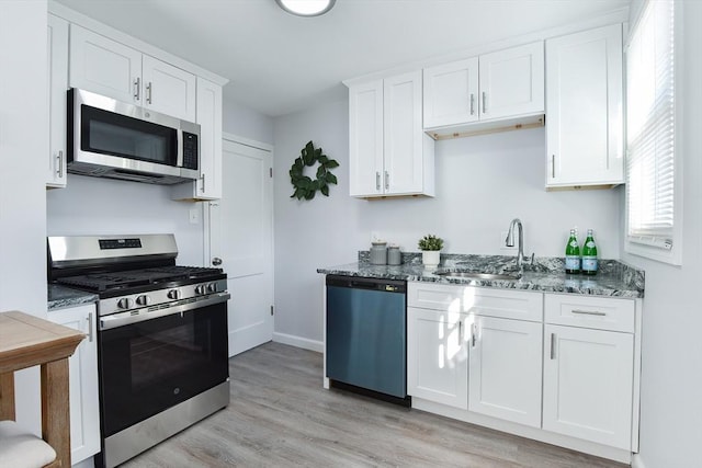 kitchen with light wood-style flooring, a sink, dark stone countertops, stainless steel appliances, and white cabinets