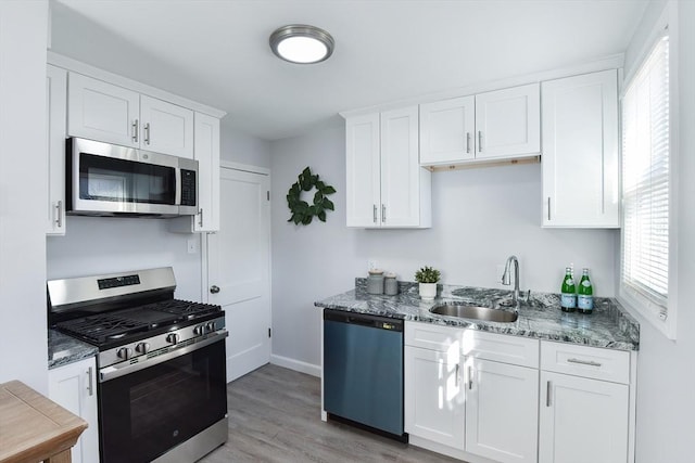 kitchen with light wood-style flooring, a sink, light stone counters, stainless steel appliances, and white cabinets