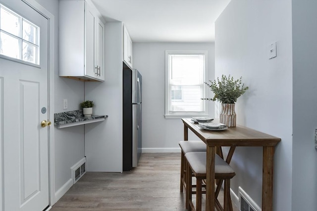 kitchen featuring a wealth of natural light, visible vents, white cabinets, and freestanding refrigerator