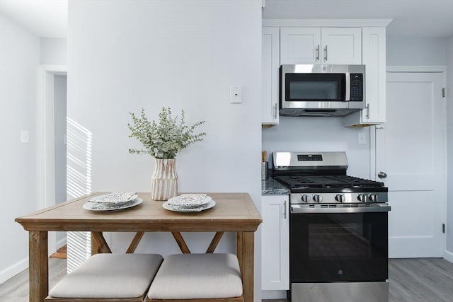 kitchen with white cabinets, baseboards, light wood-type flooring, and stainless steel appliances