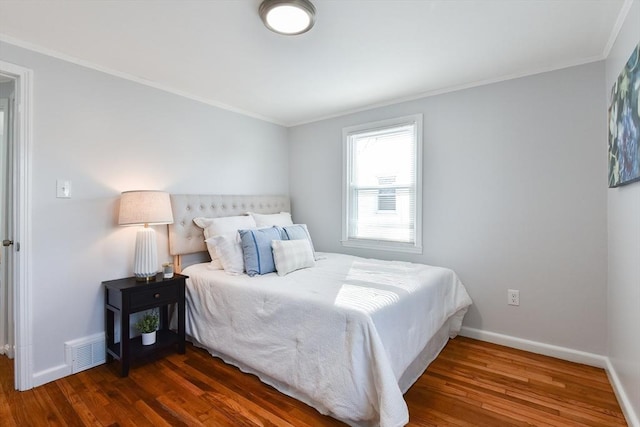 bedroom with visible vents, baseboards, wood finished floors, and crown molding