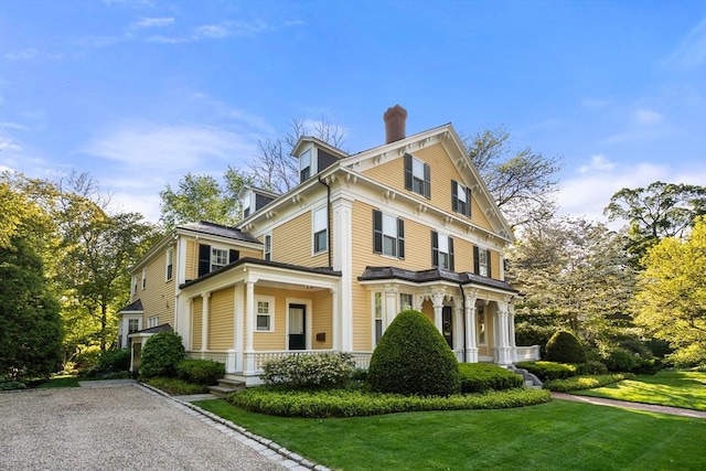 view of side of home with a chimney, a yard, and covered porch