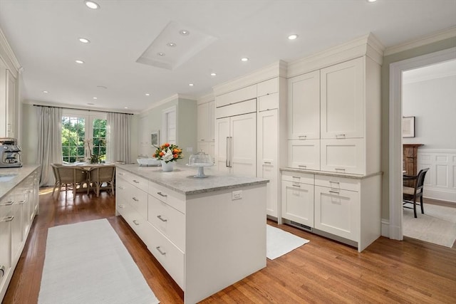 kitchen featuring crown molding, a center island, wood finished floors, white cabinetry, and light stone counters