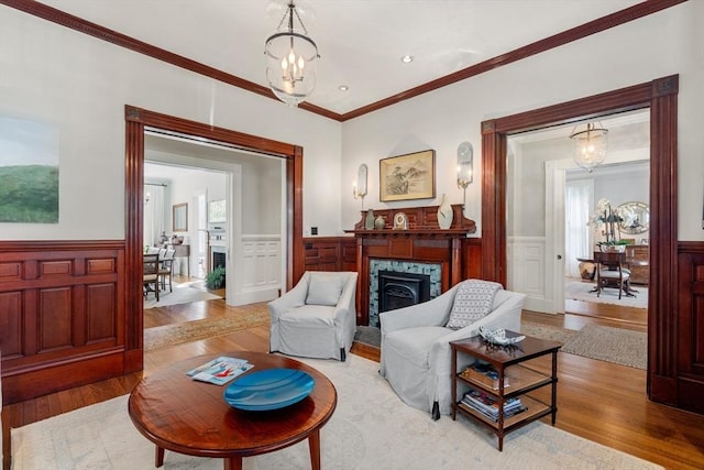 living area with a wainscoted wall, wood finished floors, a high end fireplace, ornamental molding, and a chandelier