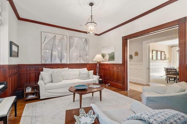 living area featuring a chandelier, wood finished floors, crown molding, and a wainscoted wall