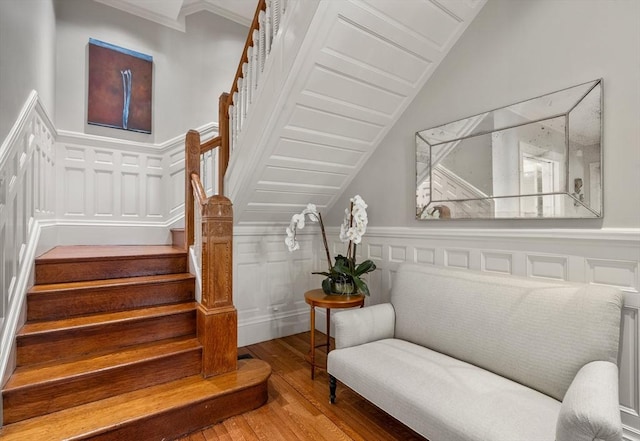 stairs with wood finished floors, crown molding, a decorative wall, a wainscoted wall, and vaulted ceiling