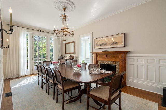 dining space with a chandelier, crown molding, light wood finished floors, a high end fireplace, and wainscoting
