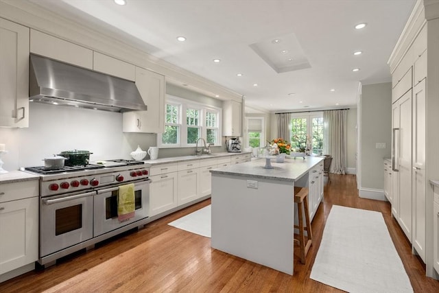kitchen with double oven range, wall chimney range hood, a center island, a sink, and plenty of natural light