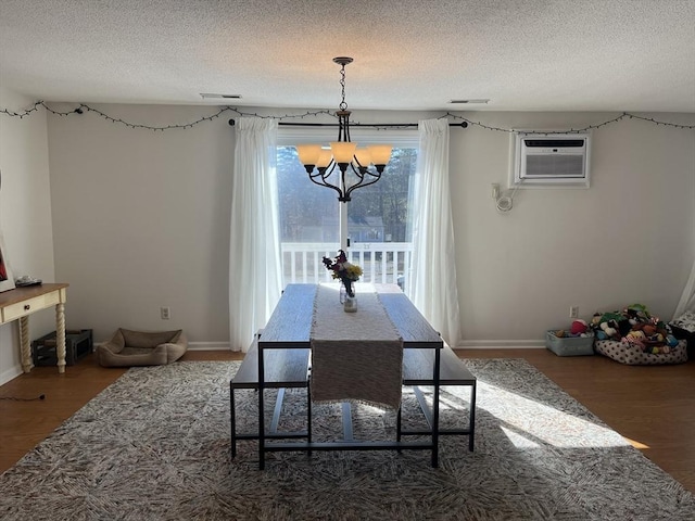 dining space with a chandelier, wood finished floors, a textured ceiling, a wall mounted air conditioner, and baseboards