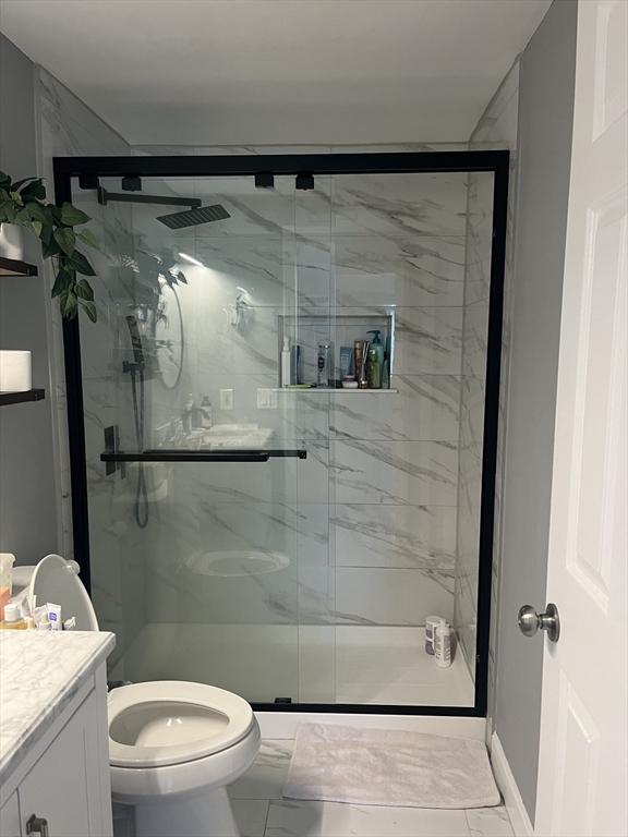 bathroom featuring vanity, marble look tiles, toilet, and a marble finish shower
