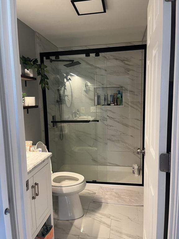 full bath with marble look tiles, toilet, a marble finish shower, and vanity