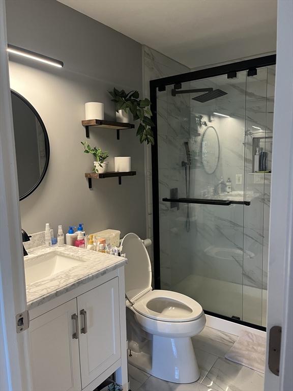 bathroom with marble finish flooring, a marble finish shower, vanity, and toilet