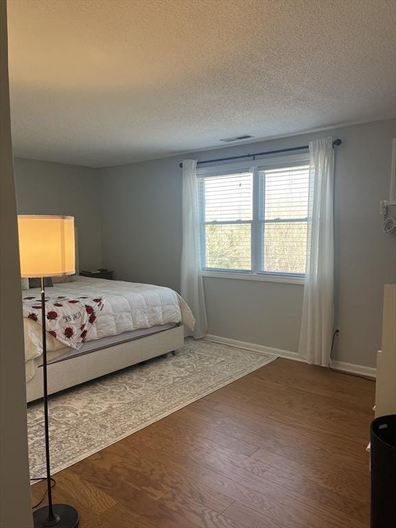 bedroom with dark wood finished floors, a textured ceiling, and baseboards